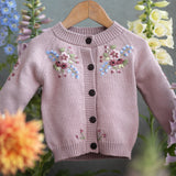 Pink embroidered cardigan on a hanger with flowers in the background