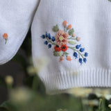 White sweater with floral embroidery on a blurred green background