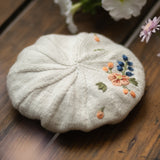 Embroidered fabric flower on a textured surface with flowers in the background