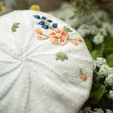 Embroidered white beret with floral patterns on a natural background