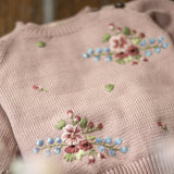 Pink sweater with floral embroidery on a wooden surface