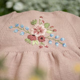 Close-up of a pink fabric with floral embroidery against a blurred natural background