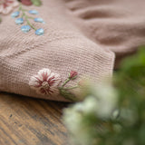 Close-up of a pink fabric with floral embroidery on a wooden surface.