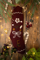 Decorative Christmas stocking with floral patterns hanging on a wooden wall with lights and ornaments.