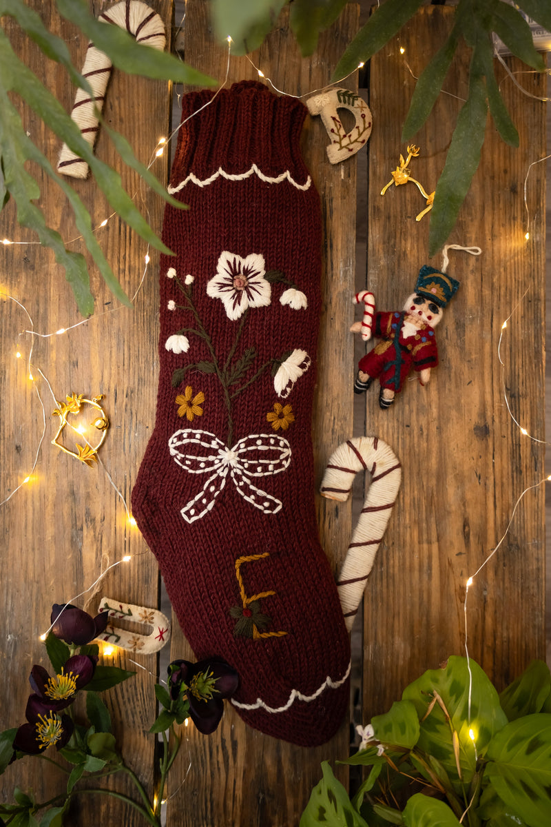 Decorative Christmas stocking with floral patterns hanging on a wooden wall with lights and ornaments.