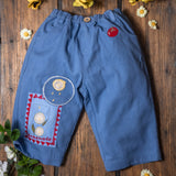 Blue children's pants with floral embroidery on a wooden surface with flowers around
