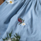 Blue dress with floral embroidery on a wooden surface with flowers in the foreground