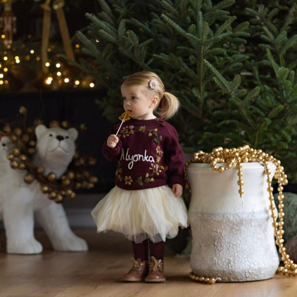 girl in front of a christmas tree wearing knitted and personalized sweater with embroidered blackberries motifs