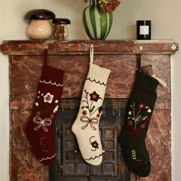 Decorative stockings hanging on a fireplace mantle with flowers in a vase.