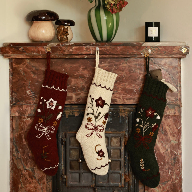 Decorative stockings hanging on a fireplace mantle with flowers in a vase.