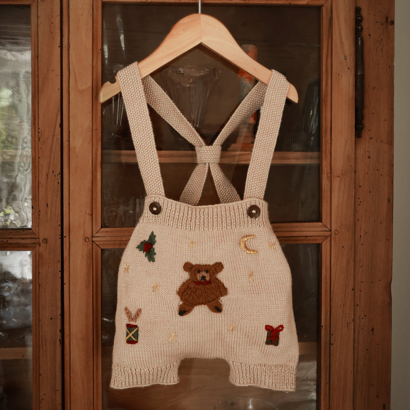 Knitted romper with bear design on a hanger in front of a wooden cabinet.