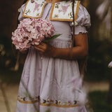 Child wearing the Birdie Bliss Dress - Lilac, holding flowers in their hands.