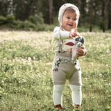 child wearing knitted mushroom bonnet and woodland suspender shorts while holding a doll