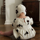 a baby girl wearing knitted and embroidered hellebore romper and a bonnet