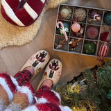 Cream Nutcracker slippers for women being worn by a person, with a Christmas tree and festive decorations visible nearby