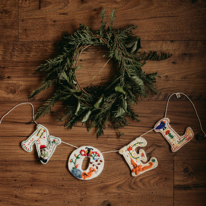 Handcrafted Noel Garland displayed with a green wreath above, emphasizing its festive charm and integration with holiday decor.