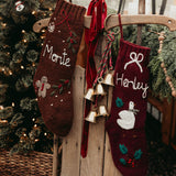 Two Christmas stockings with names 'Monte' and 'Herley' hanging on a wooden chair next to a decorated tree.