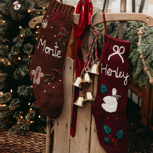 Two Christmas stockings with names 'Monte' and 'Herley' hanging on a wooden chair next to a decorated tree.