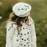 Person wearing a white embroidered beret and cardigan in a natural setting
