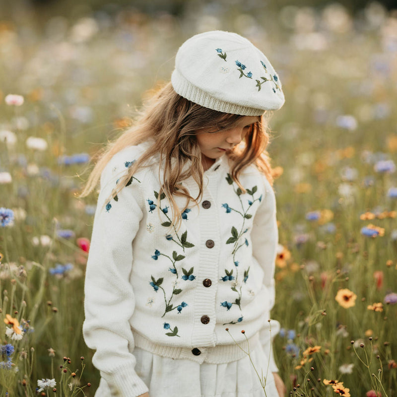 Child in a white sweater and hat standing in a field of wildflowers with a blurred background