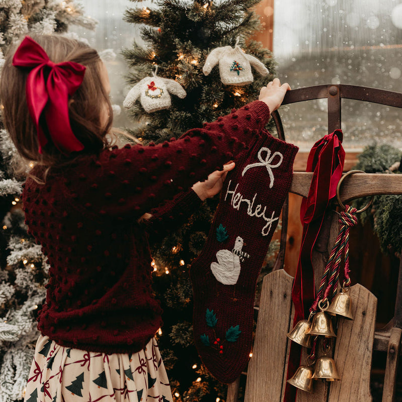 Child holding a personalized Christmas stocking in front of a decorated tree.