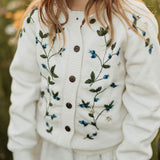 White cardigan with blueberries embroidery worn by a person in a field of flowers