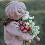 Person wearing a pink knit hat and sweater holding a bouquet of flowers in a field.
