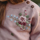 Close-up of a pink sweater with floral embroidery and brown buttons.
