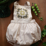 Baby romper with geometric pattern on a wooden surface with greenery