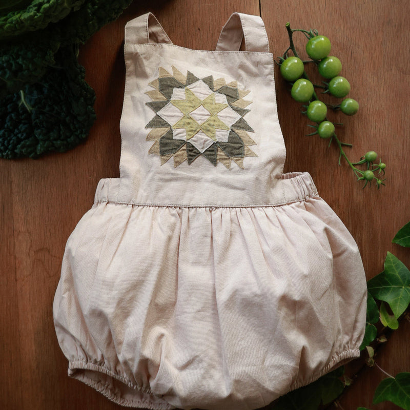 Baby romper with geometric pattern on a wooden surface with greenery