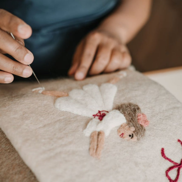 Close-up of embroidered Odette on cream white holiday stocking, highlighting detailed handcrafting and punch needle details.