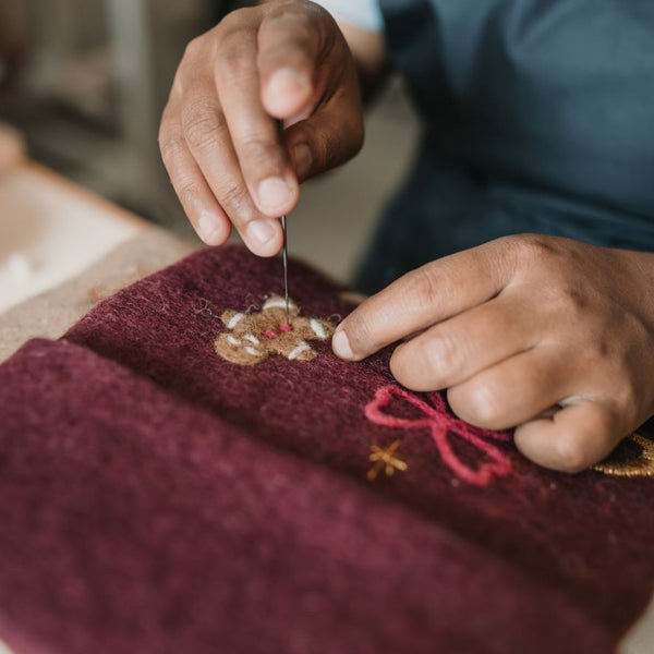 Close-up of personalized embroidered gingerbread on dark grape holiday stocking, highlighting meticulous craftsmanship and punch needle details.