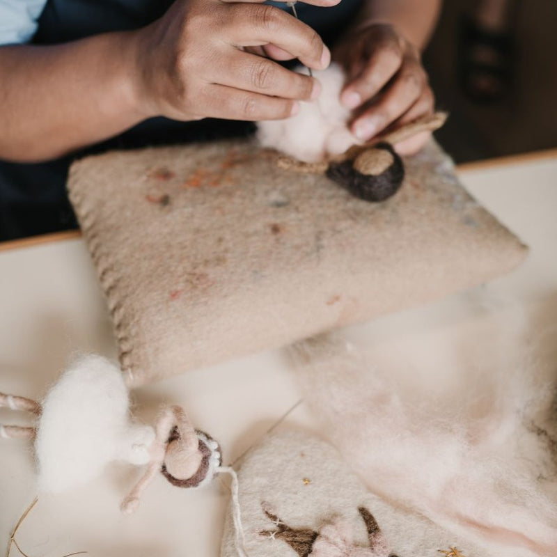 Artisan working on the creation of a white hand-felted ballerina ornament, showcasing the wool felting process and delicate craftsmanship involved.