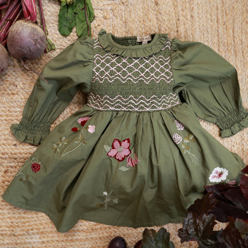 Green dress with floral embroidery on a textured surface with vegetables