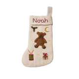 Personalized cream white holiday stocking with embroidered teddy bear and custom name, hanging on a mantel. Showcases intricate handcrafting and festive charm.