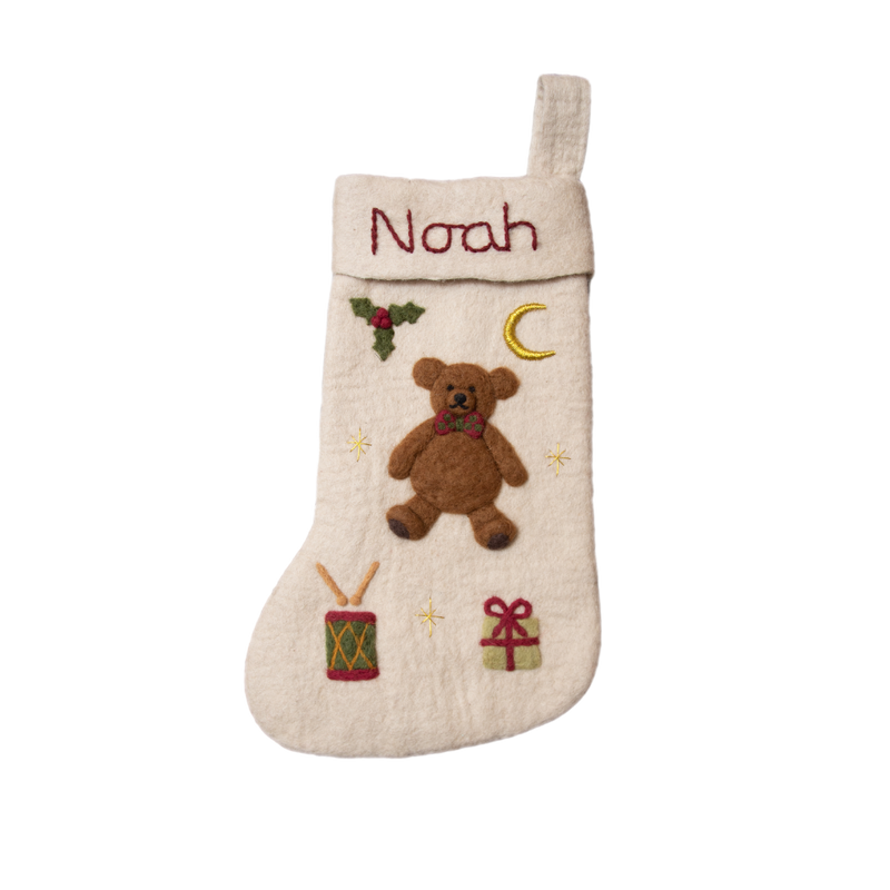 Personalized cream white holiday stocking with embroidered teddy bear and custom name, hanging on a mantel. Showcases intricate handcrafting and festive charm.