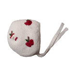 A cream white wool bonnet with hand-embroidered red apples and soft ties.
