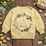 Yellow sweater with floral and bird design on a wooden surface with Easter decorations.