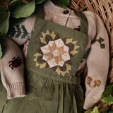wooden background with a green romper and quilted pattern, surrounded by leaves and berries.