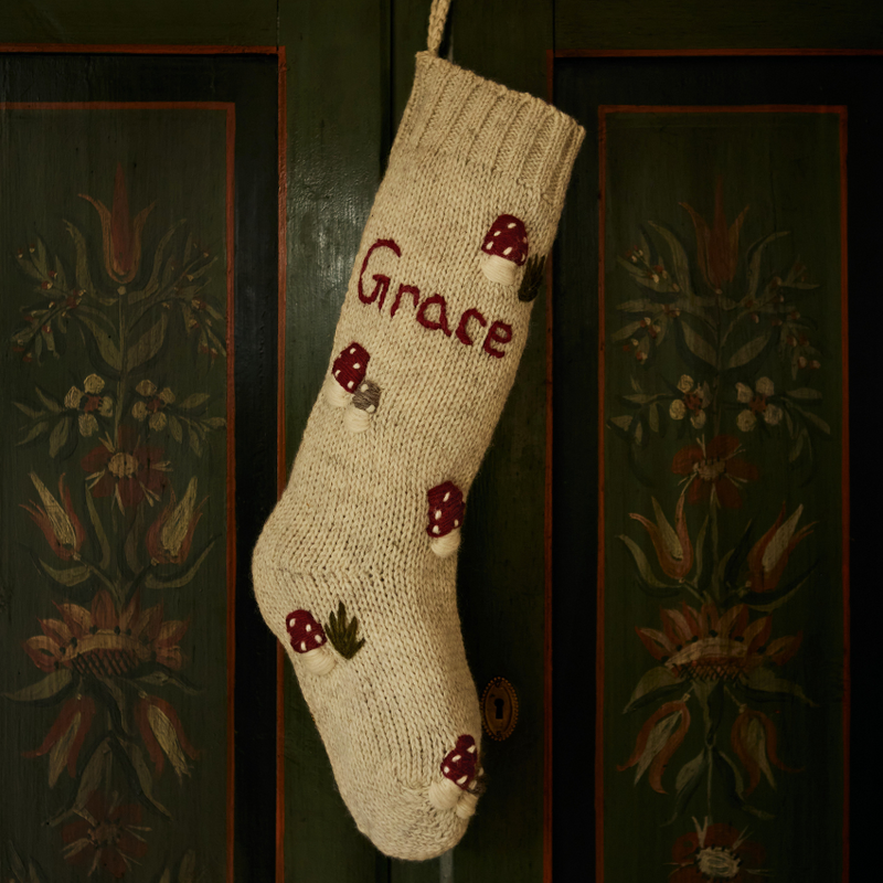  Close-up of the rye-colored personalized wool stocking with a hand-embroidered mushroom pattern, hanging partially on a wardrobe.