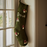 Moss-colored personalized wool stocking with a hand-embroidered mushroom pattern, hanging near a window.