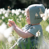 Child wearing a knitted bonnet with bird design in a field of white flowers