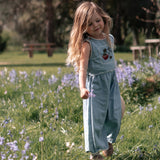 Young girl in a denim dress standing in a field of flowers with trees in the background