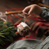 Handcrafted Gingerbread House Ornament in brown, held in hands with soft focus on the background






