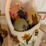 Decorative basket with felted animals and flowers on a white surface