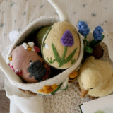 Toy basket with embroidered eggs, a duck, and other small toys on a textured surface.