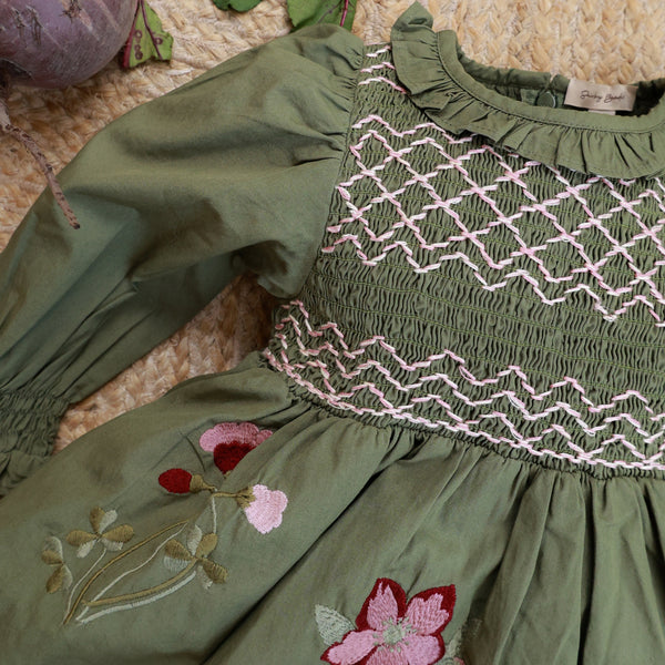 Green dress with floral embroidery on a textured surface with vegetables.