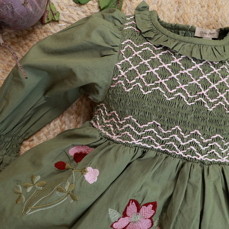 Green dress with floral embroidery on a textured surface with vegetables.