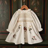 White embroidered dress on a hanger against a decorative wall.
