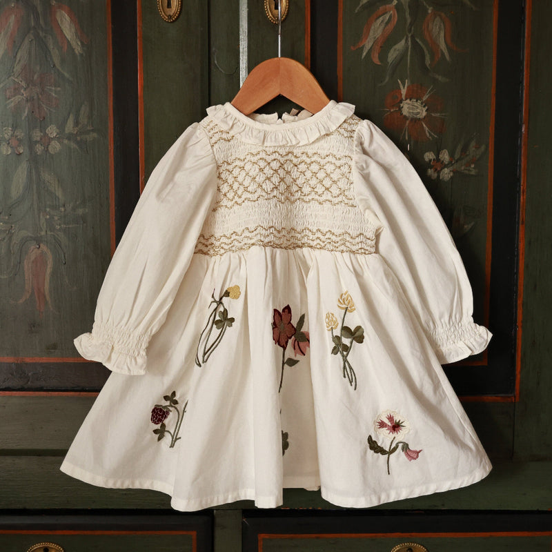 White embroidered dress on a hanger against a decorative wall.